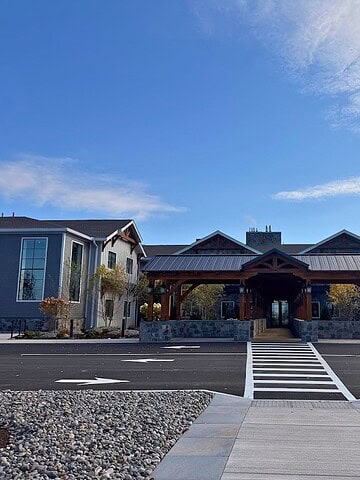 A modern building with a wood entrance, stone accents, and a crosswalk leading up to it under a blue sky at Skaneateles Fields Resort Spa—perfect for your next getaway. Read our skaneateles-fields-resort-spa-review for more insights.