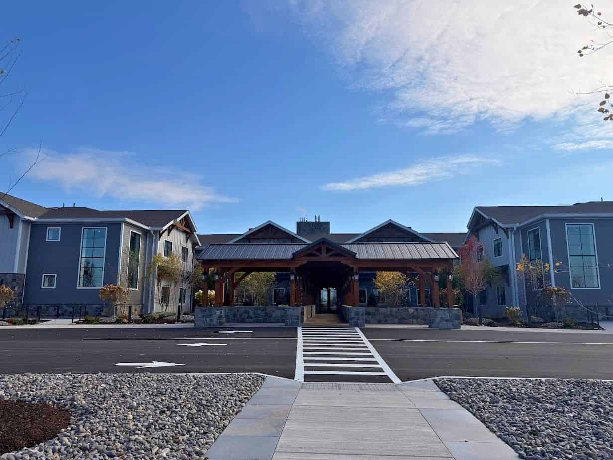 A modern building with a wood entrance, stone accents, and a crosswalk leading up to it under a blue sky at Skaneateles Fields Resort Spa—perfect for your next getaway. Read our skaneateles-fields-resort-spa-review for more insights.