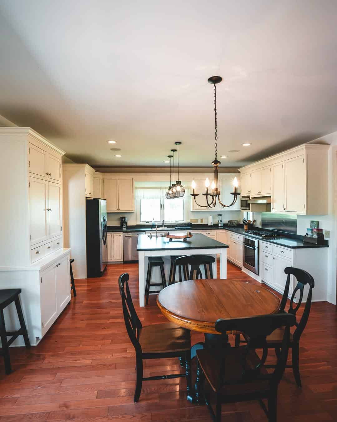 Spacious kitchen with white cabinets, a center island, round wooden table, and black chairs on wood flooring&mdash;perfect for relaxing after exploring Finger Lakes Wineries with Lodging.
