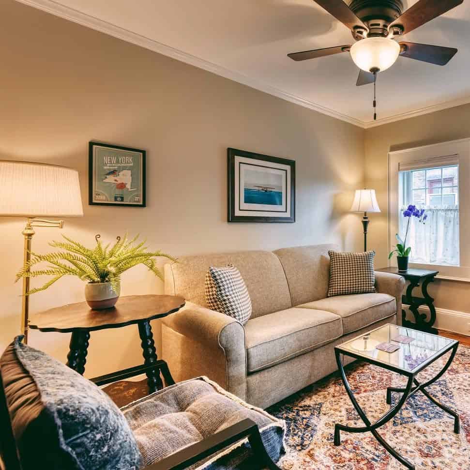Cozy living room with a beige sofa, glass coffee table, armchair, lamps, and framed wall art&mdash;perfect for relaxing after touring Finger Lakes Wineries with Lodging nearby.