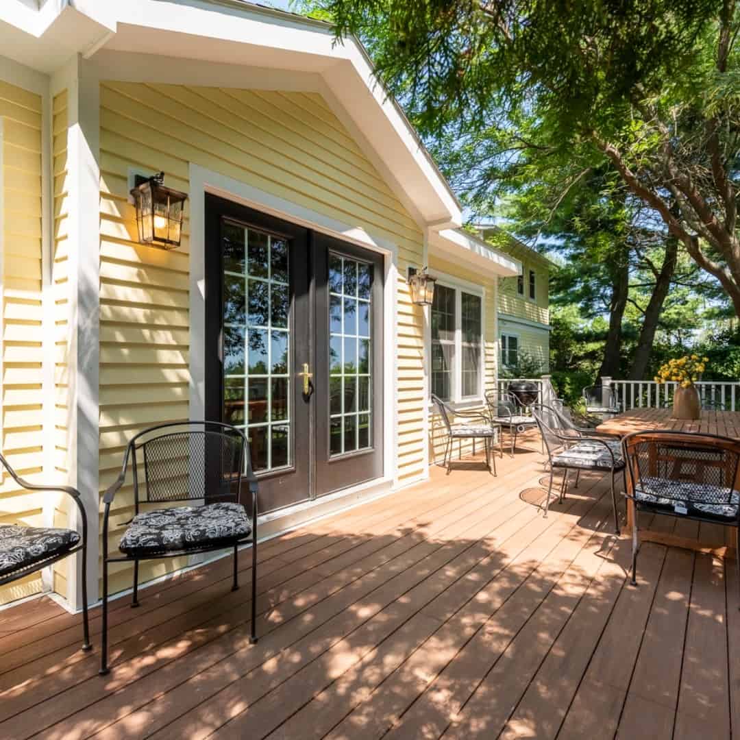 Sunny outdoor patio with black chairs, a table, and double glass doors on a yellow house with trees nearby&mdash;ideal for relaxing after a day exploring Finger Lakes Wineries with Lodging.