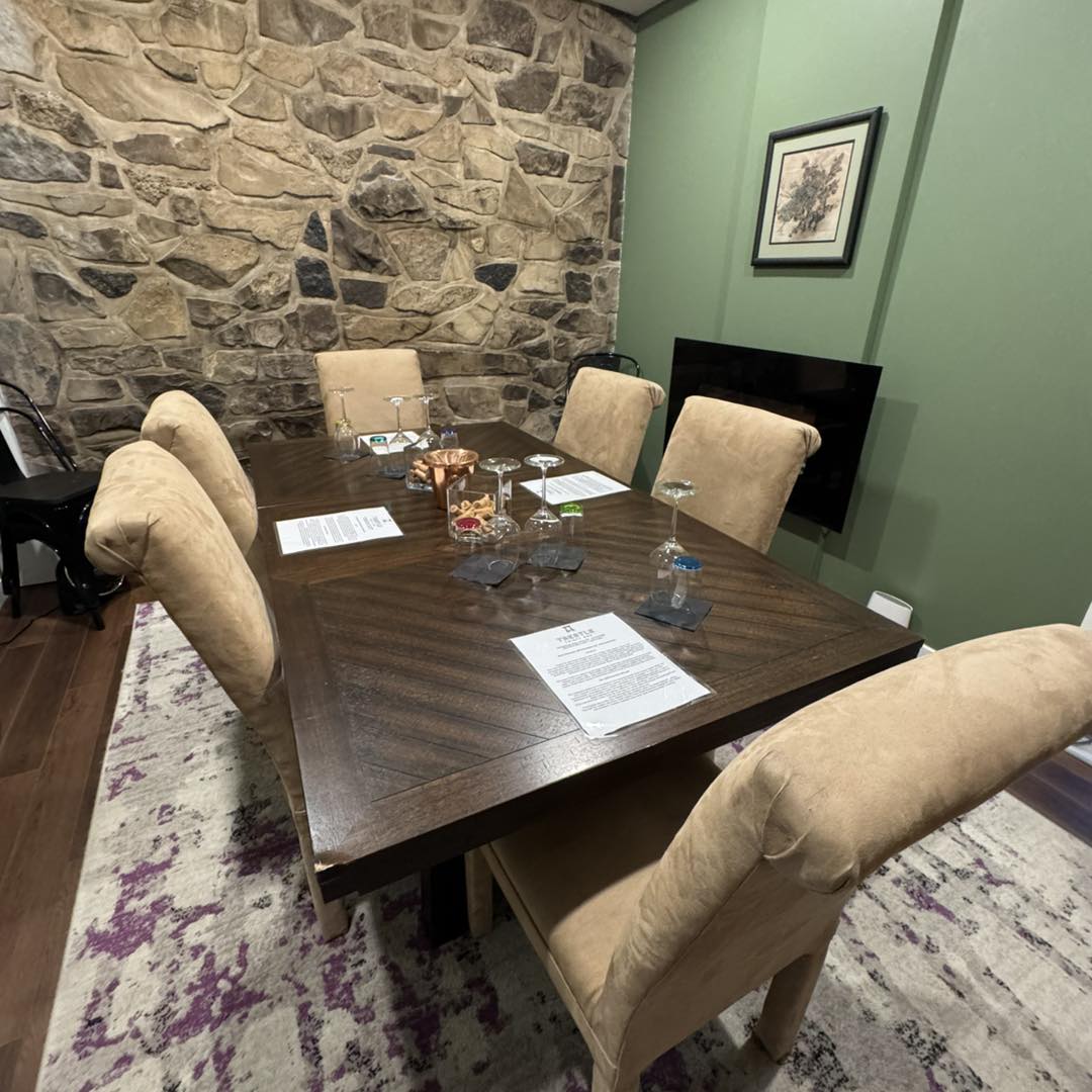 A wooden dining table with beige chairs, papers, glasses, and snacks evokes the relaxed charm of tasting rooms at the best wineries in Finger Lakes, set in a room with stone and green walls.