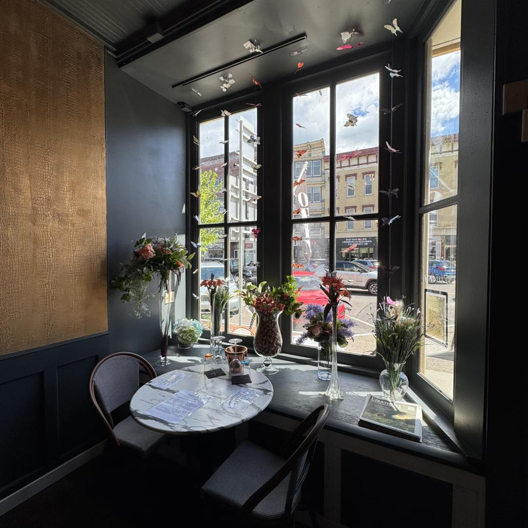 A sunlit café corner with a marble table, two chairs, and various flower arrangements by a large window—perfect for planning your next visit to the best wineries in Finger Lakes.