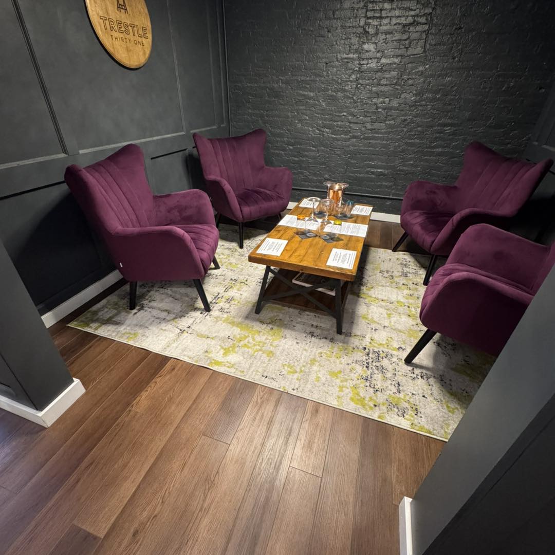 Four purple armchairs surround a wooden coffee table on a rug in a modern, dark-walled room—perfect for savoring selections from the best wineries in Finger Lakes.