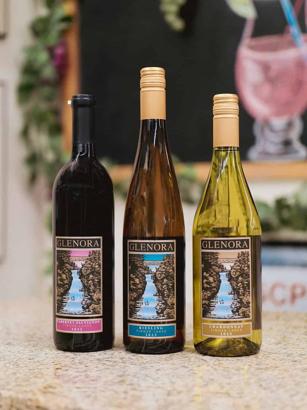 Three Glenora wine bottles&mdash;Cabernet Sauvignon, Riesling, and Chardonnay&mdash;on a countertop, showcasing the refined selections available at Finger Lakes Wineries with Lodging.
