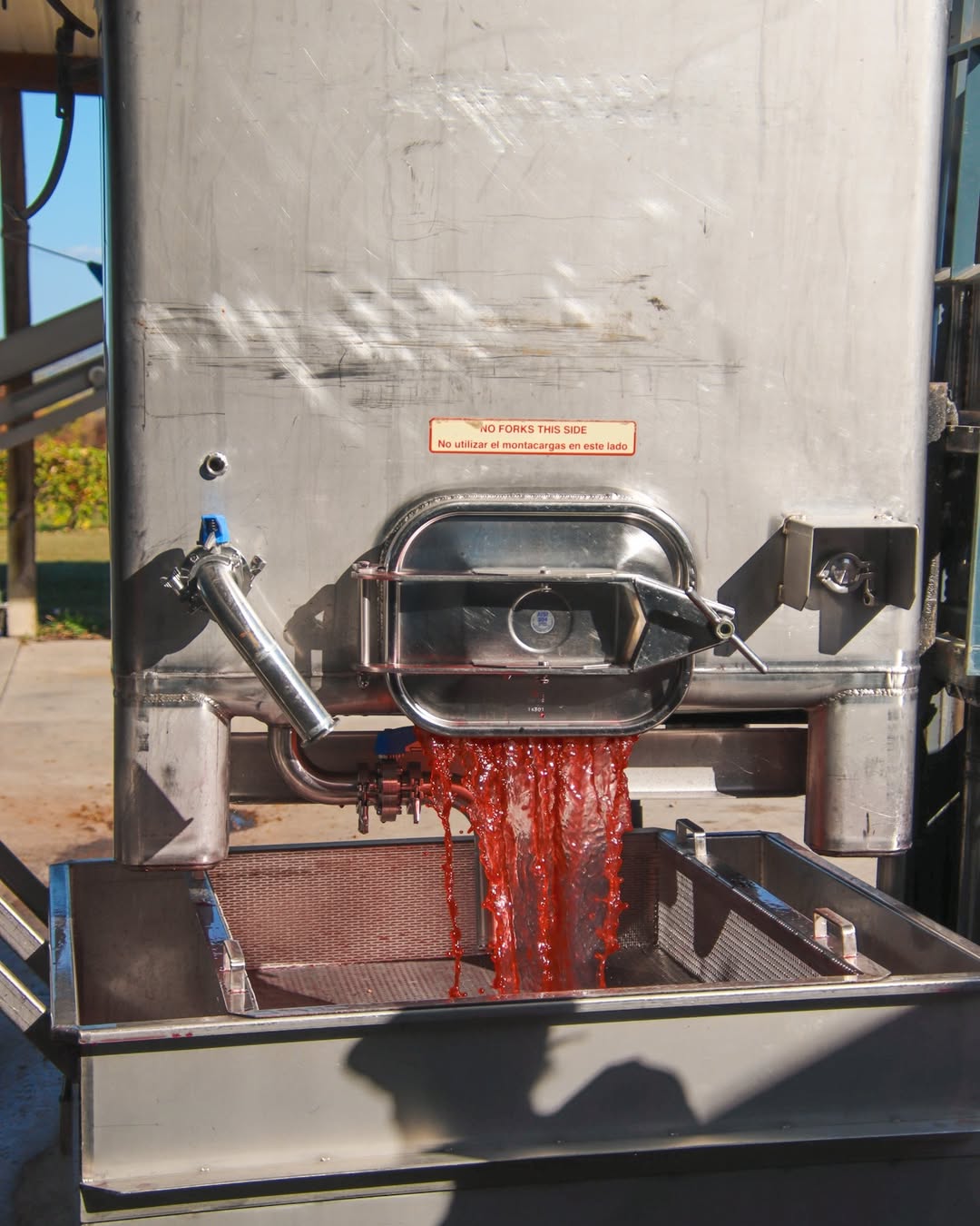 Red juice flows from a stainless steel machine into a tray during an outdoor winemaking process at one of the best wineries in Finger Lakes.