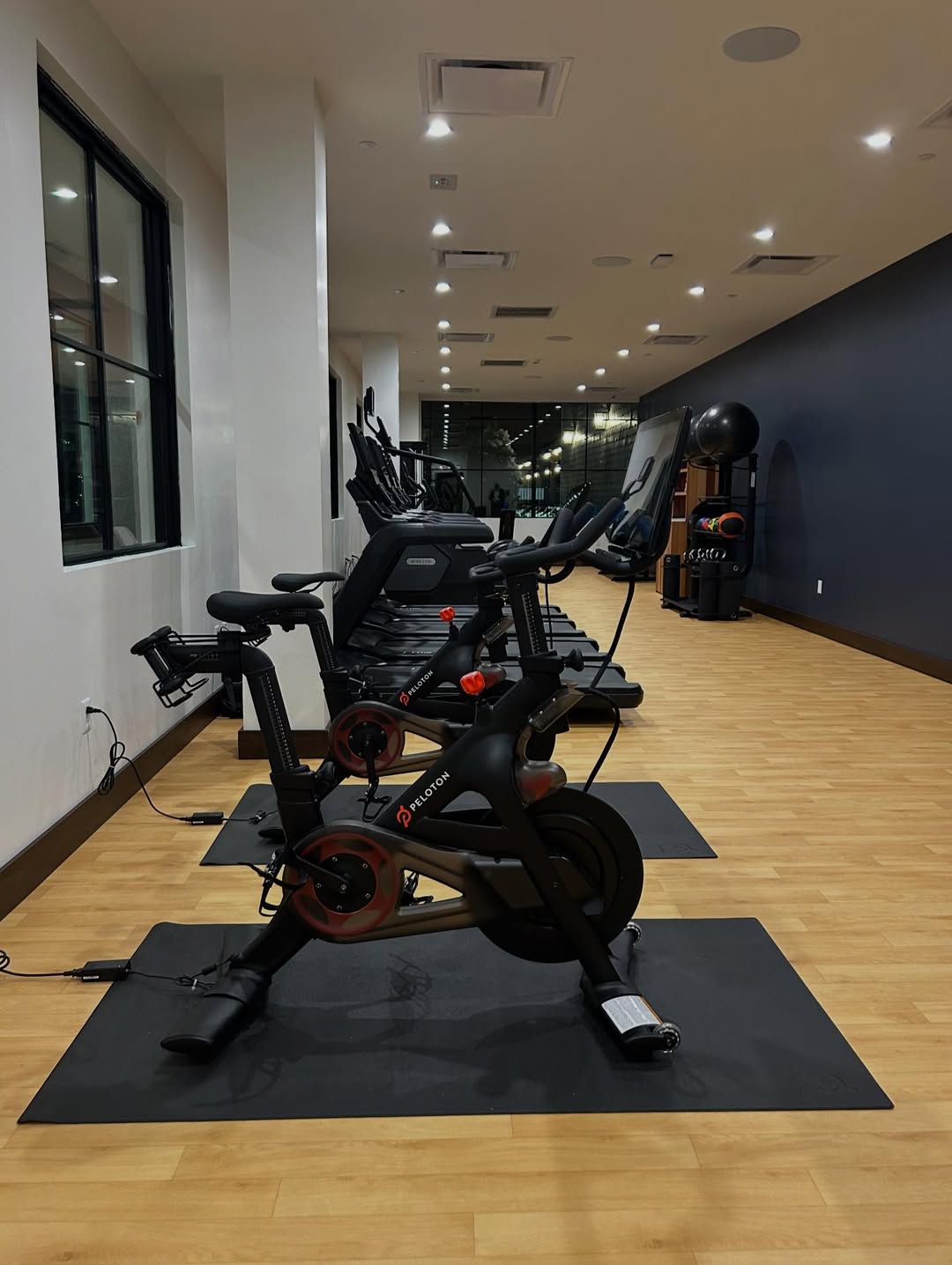 A modern gym at Skaneateles Fields Resort features stationary bikes, treadmills, and exercise equipment on a sleek wooden floor—perfect for staying active during your Finger Lakes getaway.