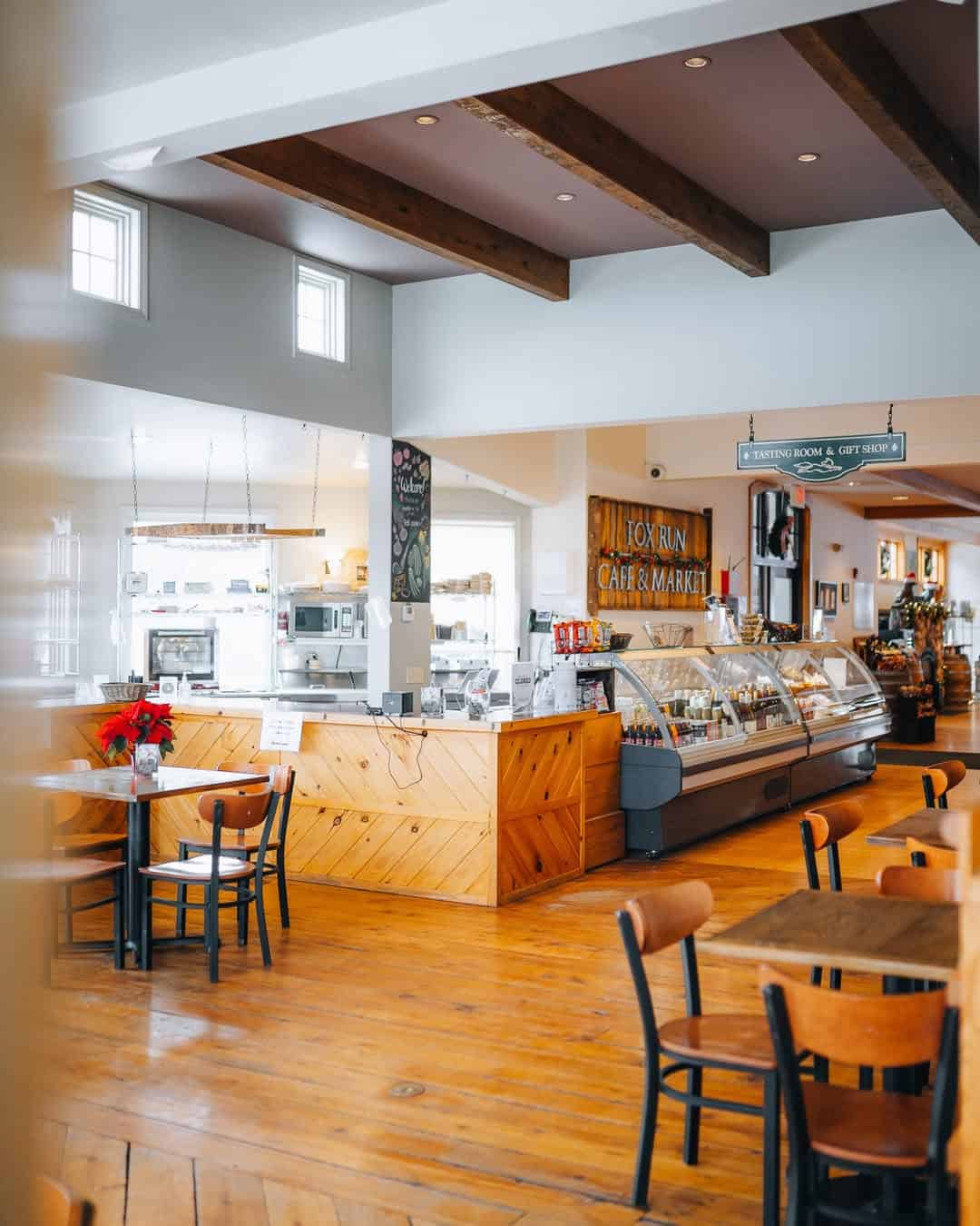 Bright, cozy caf&eacute; interior with wooden floors, tables, and a display counter under exposed ceiling beams&mdash;perfect for relaxing after exploring Finger Lakes Wineries with Lodging nearby.