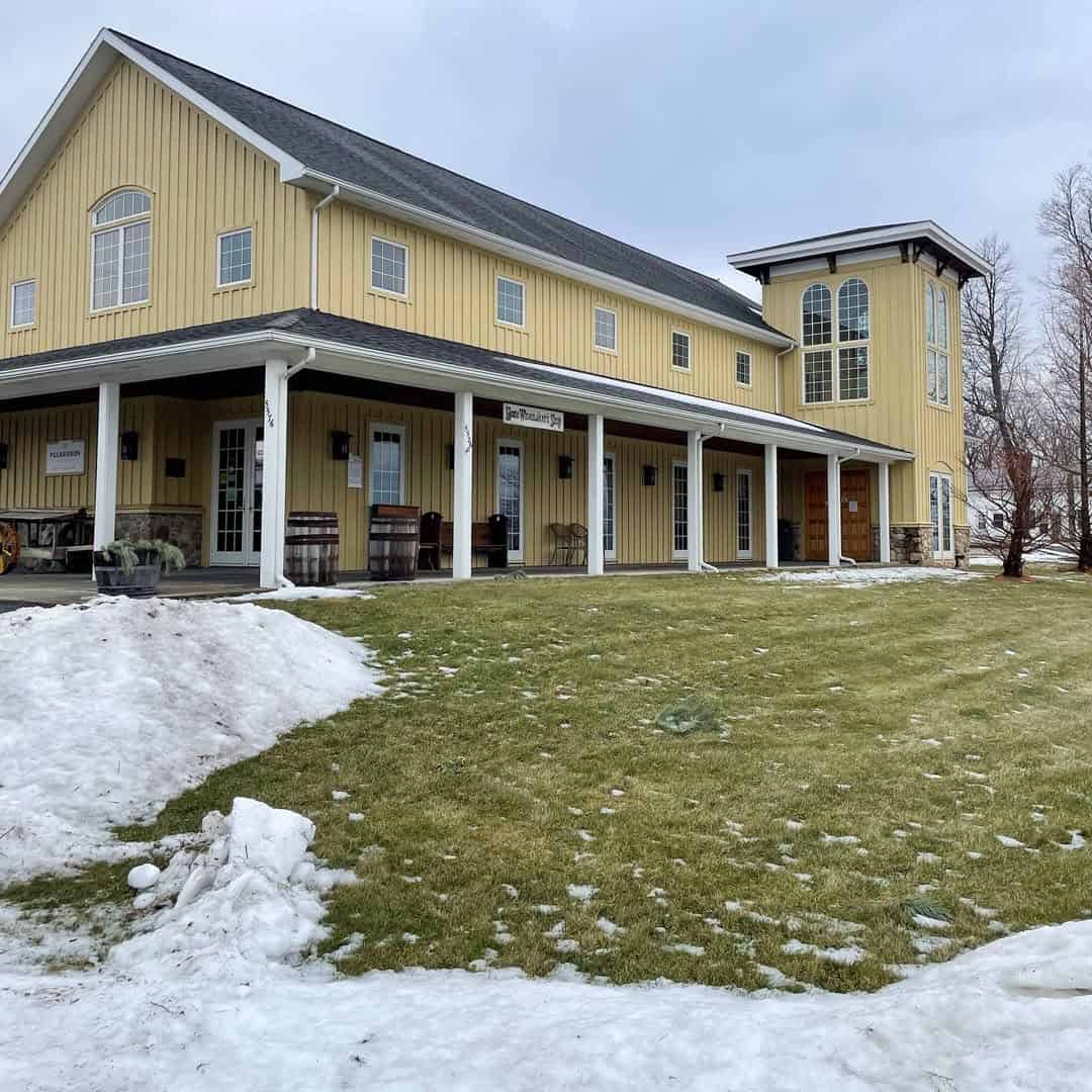 Large yellow barn-style building with tall windows, a wraparound porch, and snow on the ground&mdash;one of the charming Finger Lakes Wineries with Lodging for a cozy winter escape.