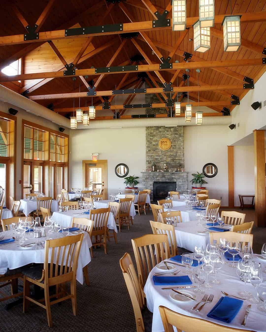 Elegant restaurant dining room with wooden ceiling, set tables, blue napkins, and large windows&mdash;perfect for guests exploring Finger Lakes wineries with lodging nearby.