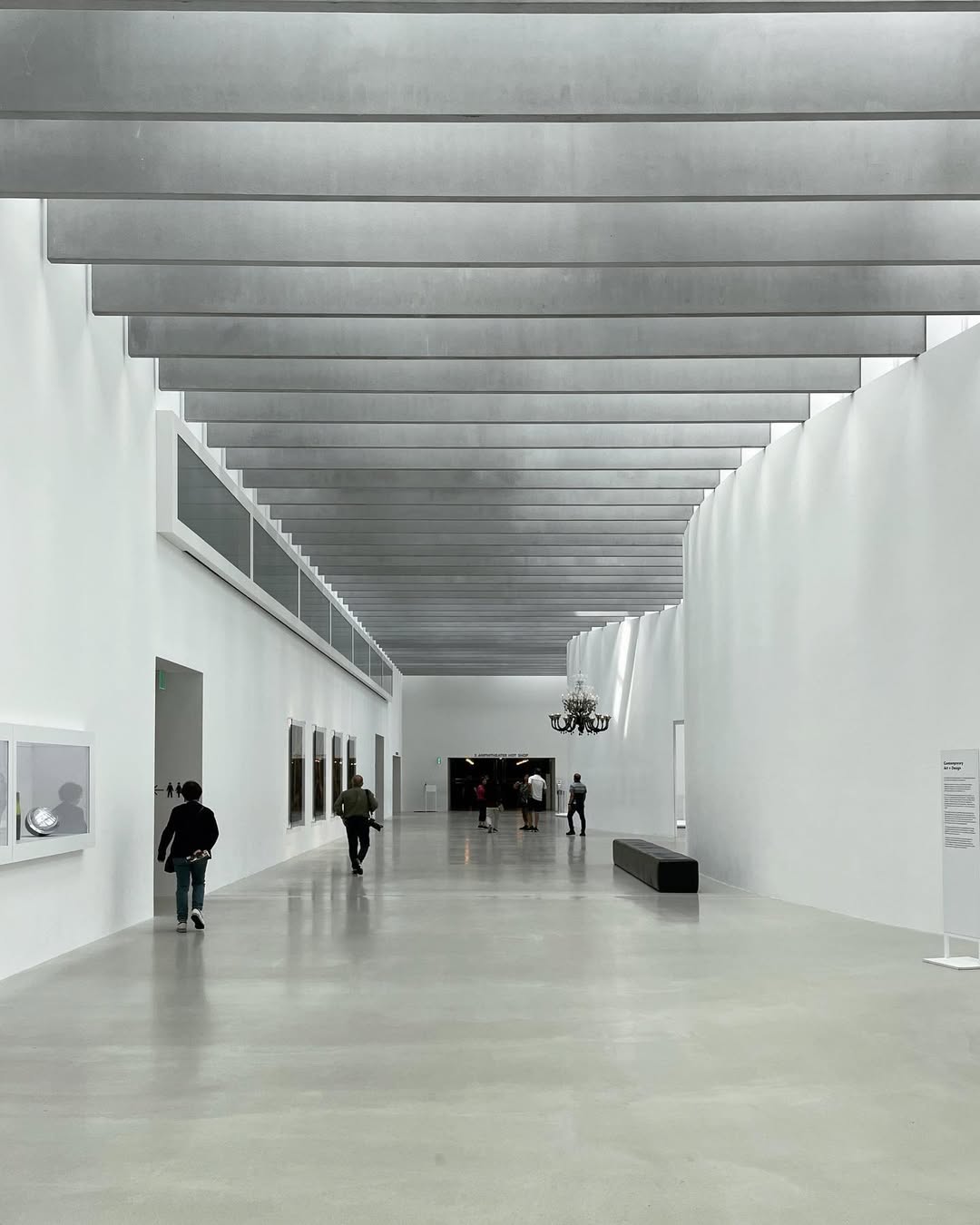 Spacious modern art gallery with high ceilings, white walls, and people walking or viewing artwork, reminiscent of the open expanses found at Watkins Glen State Park.