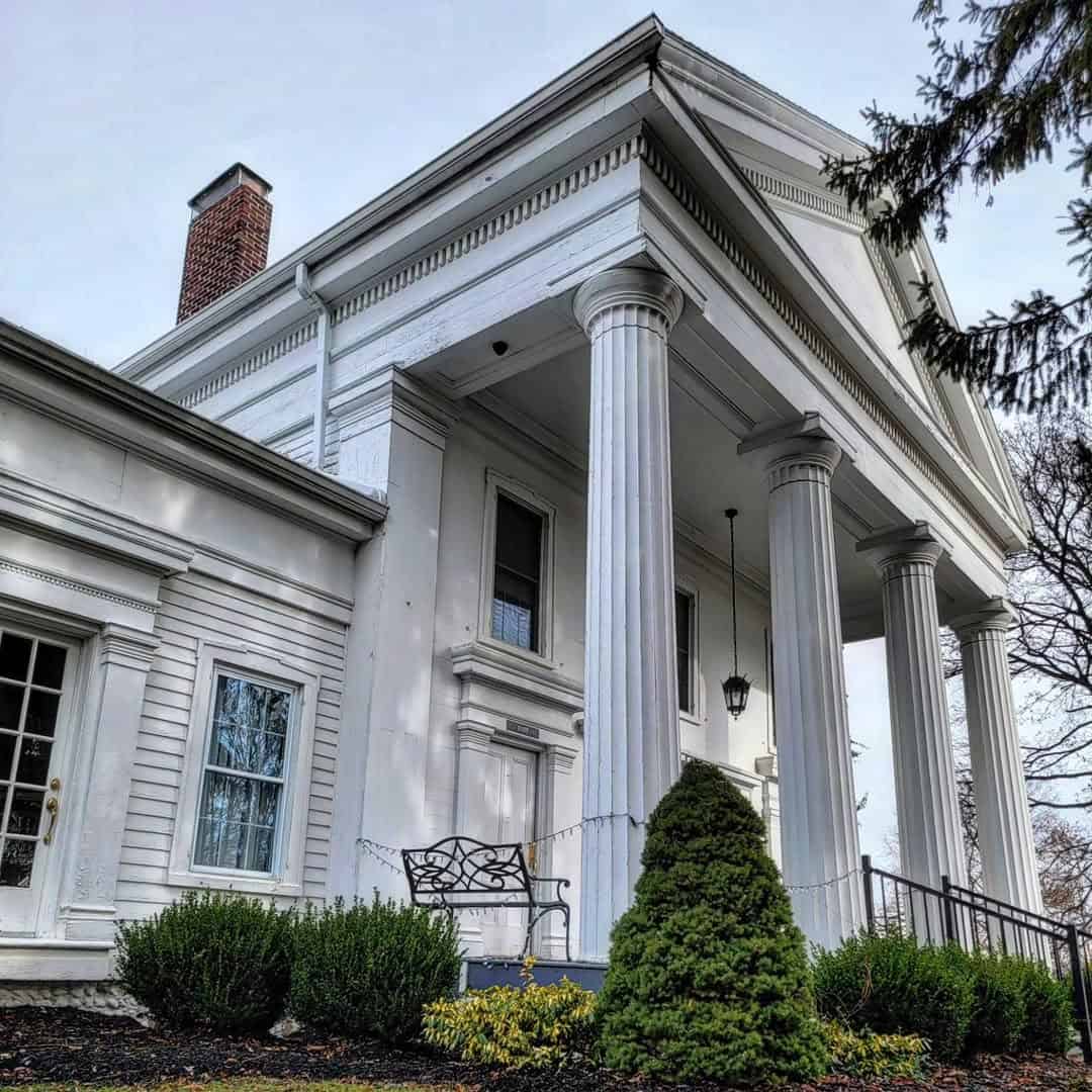White Greek Revival house with tall columns, a front porch, and trimmed green bushes in the foreground&mdash;perfect for those seeking elegant stays while exploring Finger Lakes Wineries with Lodging.