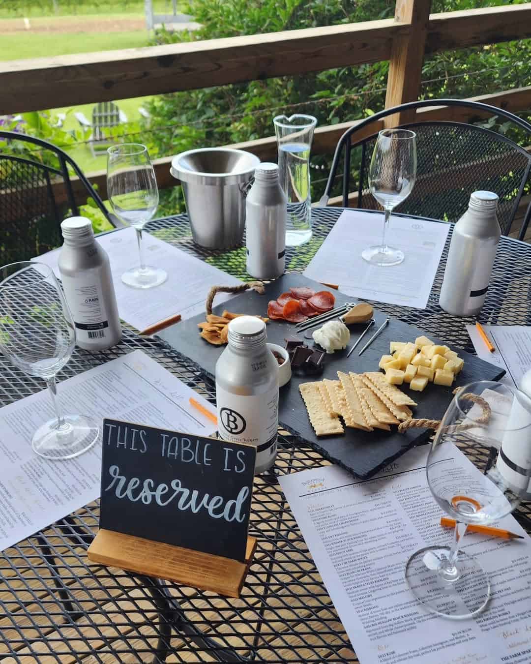Outdoor table featuring wine glasses, bottled drinks, cheese platter, menus, and a "reserved" sign&mdash;perfect for guests enjoying the charm of Finger Lakes Wineries with Lodging.