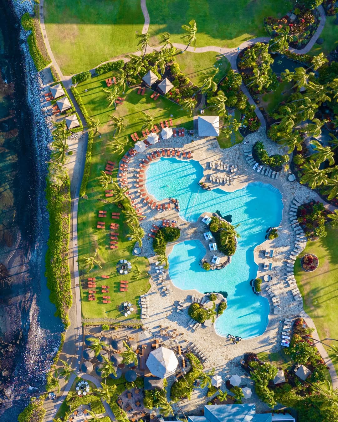 Aerial view of one of the best family resorts with large pools, lounge chairs, palm trees, and green lawns by the ocean.