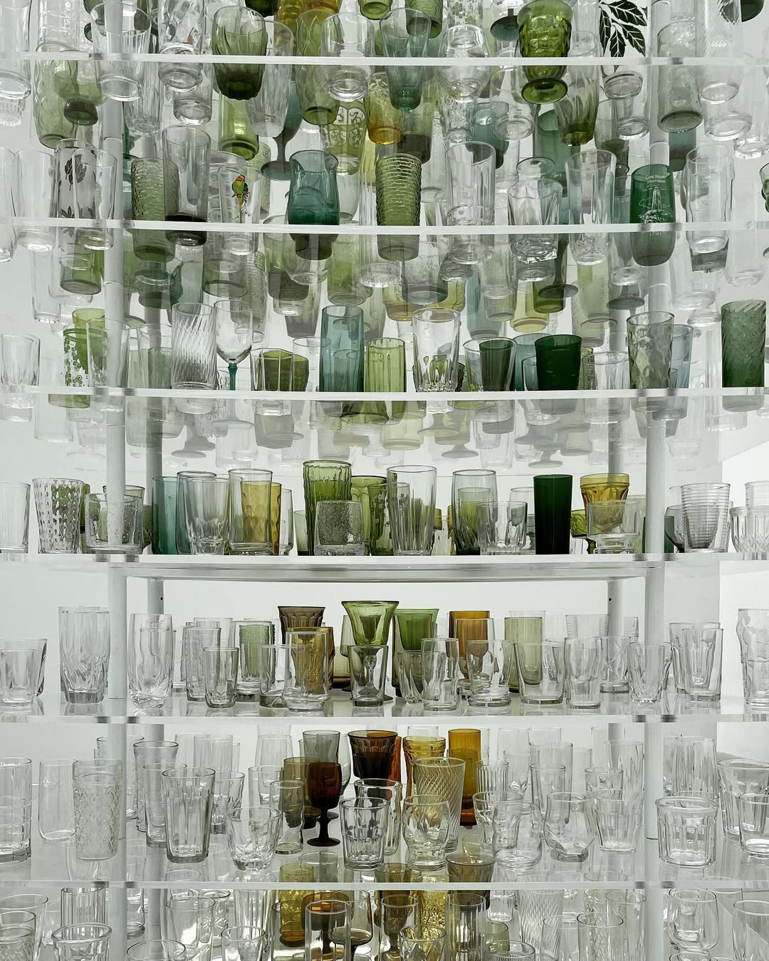 Shelves filled with various clear and green glass cups, goblets, and tumblers arranged in rows evoke the timeless charm of a gift shop near Watkins Glen State Park.