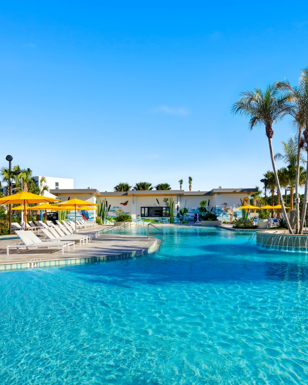 Outdoor swimming pool with clear blue water, lounge chairs, yellow umbrellas, and palm trees under a sunny sky&mdash;perfect for relaxing at one of the best family resorts or top family vacation spots.