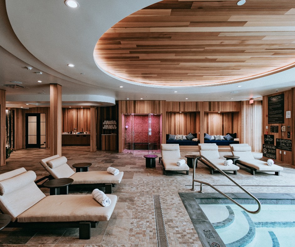 Modern spa lounge at Skaneateles Fields Resort with cushioned chairs, rolled towels, and a pool under a curved wooden ceiling—an inviting retreat in the heart of the Finger Lakes.