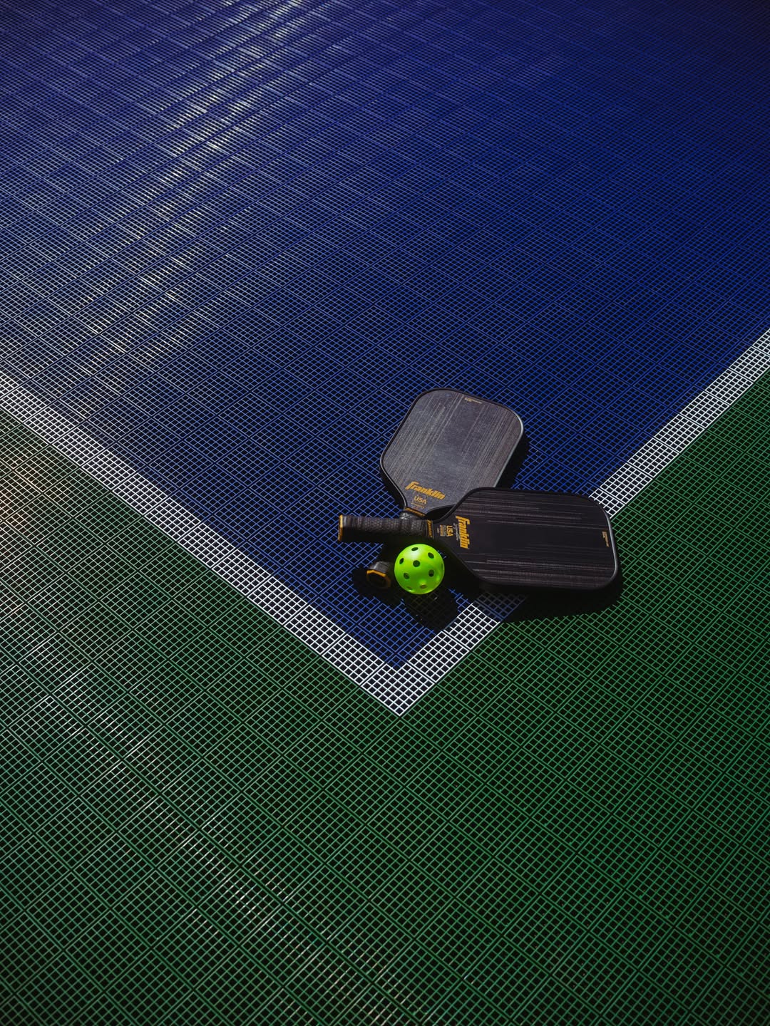 Two pickleball paddles and a ball rest on the blue and green corner of the court at Skaneateles Fields Resort, capturing a moment of leisure in the heart of the Finger Lakes.
