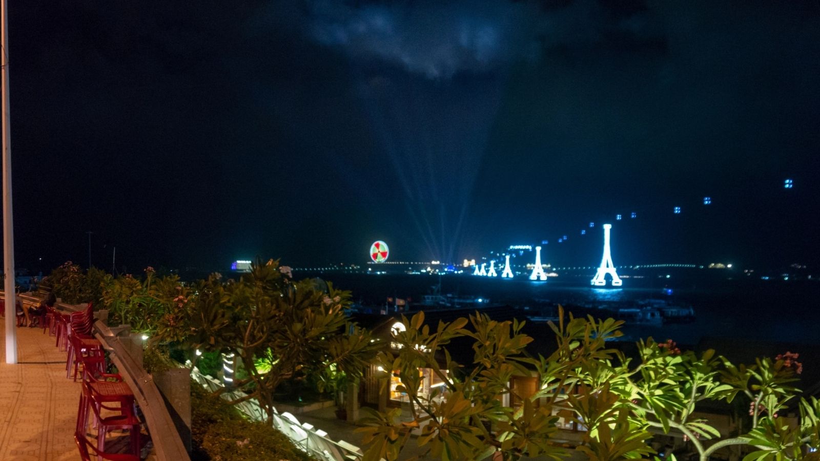 Outdoor terrace at night with illuminated trees, empty chairs, and bright lights over water in the distance—a perfect spot to relax and unwind after a day of exploring with your favorite Asia travel tips.