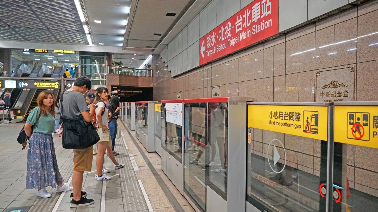 People waiting on a subway platform at Taipei Main Station, with safety signs and glass barriers visible—one of the best Asia travel hacks is to seek shelter here during hot weather while exploring the city.