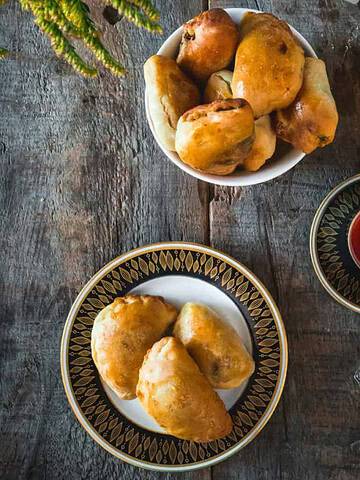 A plate of baked pastries, inspired by vegetarian dishes in Russia, with a cup of tea and a bowl of more pastries on a rustic wooden table.
