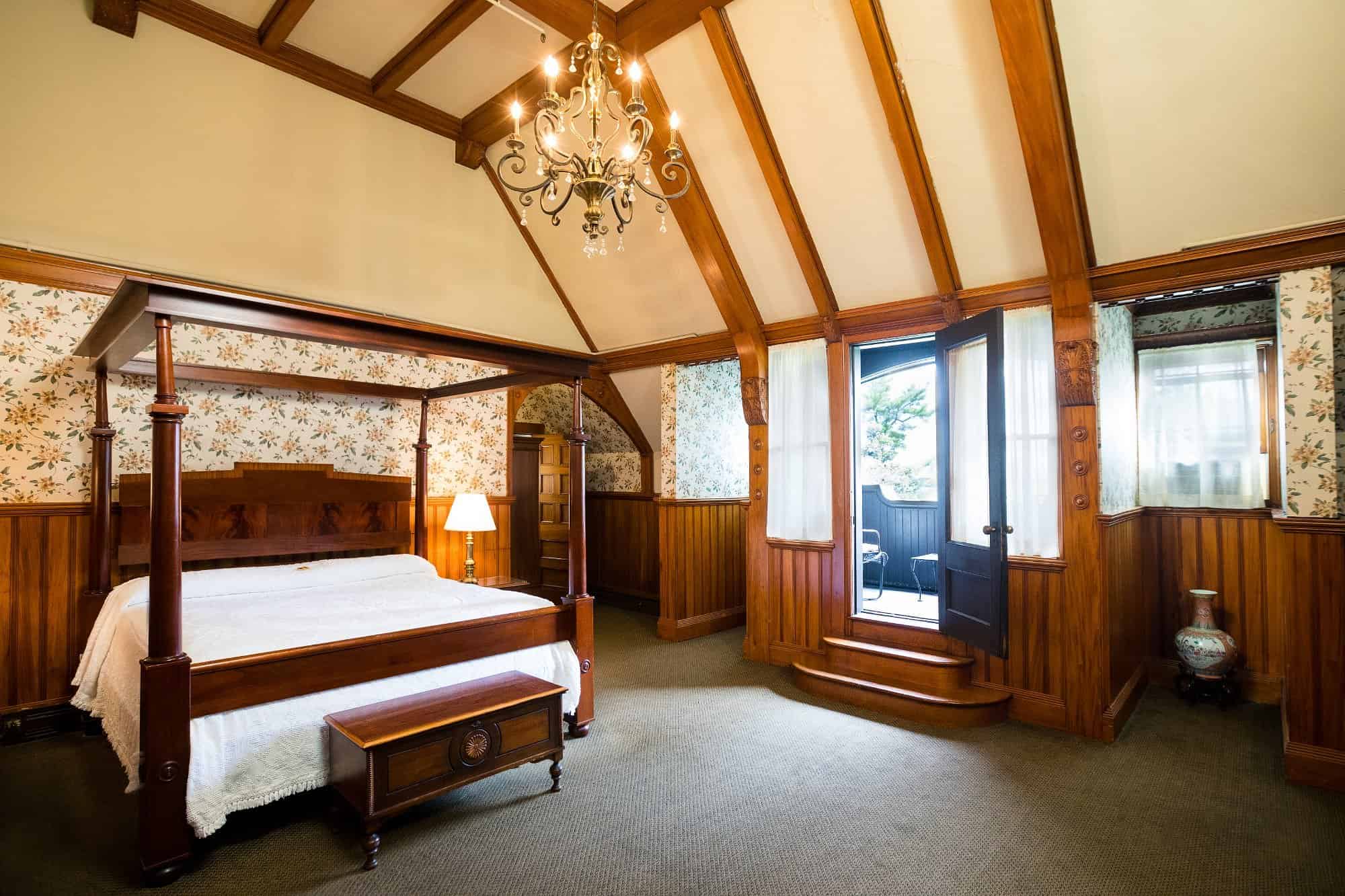 Spacious, wood-paneled bedroom with a canopy bed, chandelier, floral wallpaper, and door to a balcony&mdash;perfect for relaxing after exploring Finger Lakes wineries with lodging nearby.
