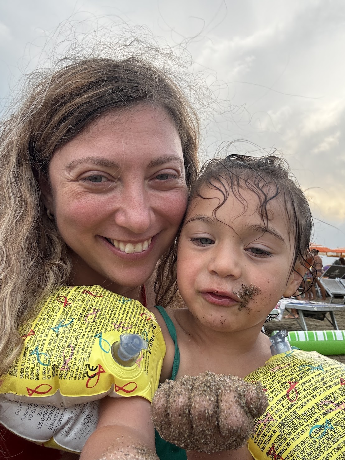 Smiling woman and child in yellow floaties; child has wet hair and sand on face and hand, enjoying a sunny day outdoors at one of the top family resorts.