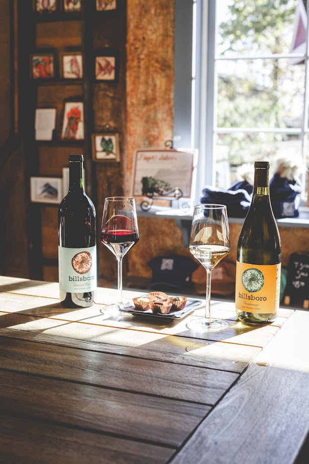Two bottles of Billsboro wine from one of the best wineries in Finger Lakes, two glasses, and snacks sit on a wooden table by a sunny window.