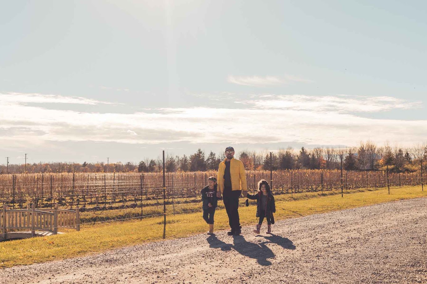 Person in a yellow jacket walking on a gravel path with two children in a sunny, rural landscape near some of the best wineries in Finger Lakes.