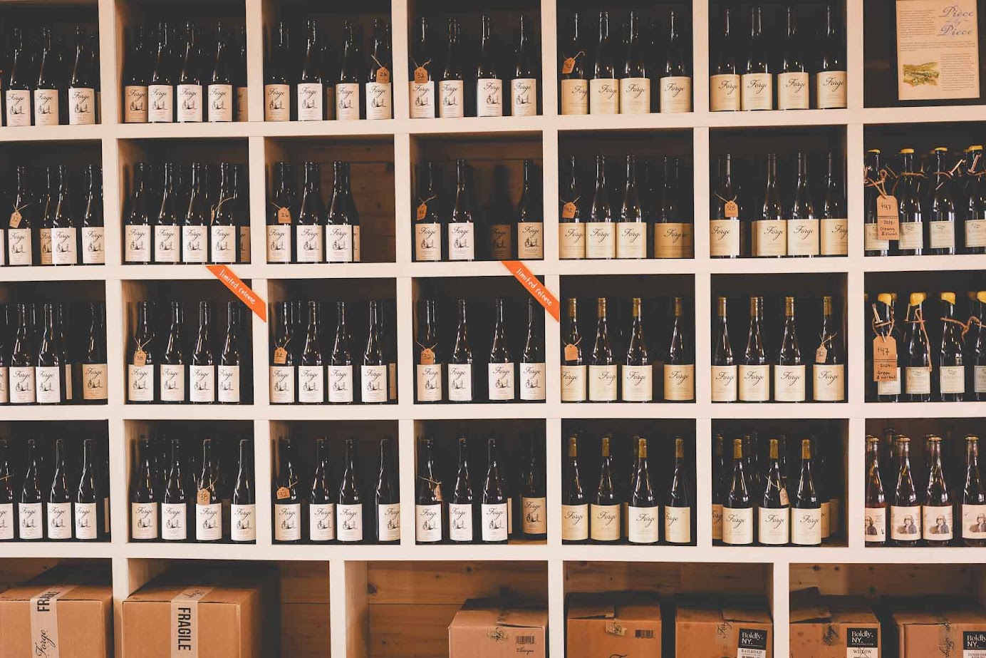 Shelves filled with neatly arranged wine bottles and boxes from some of the best wineries in Finger Lakes, displayed in a wine shop or cellar.
