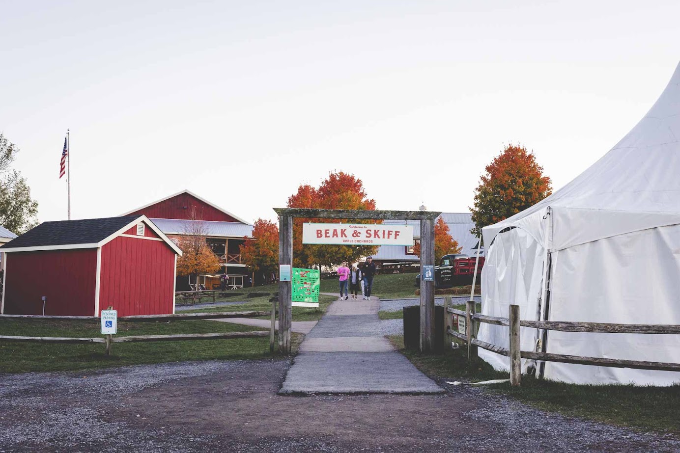 Outdoor entrance to Beak & Skiff with red buildings, autumn trees, and a white tent—an inviting stop for a fall road trip through the Finger Lakes or a relaxing weekend getaway.