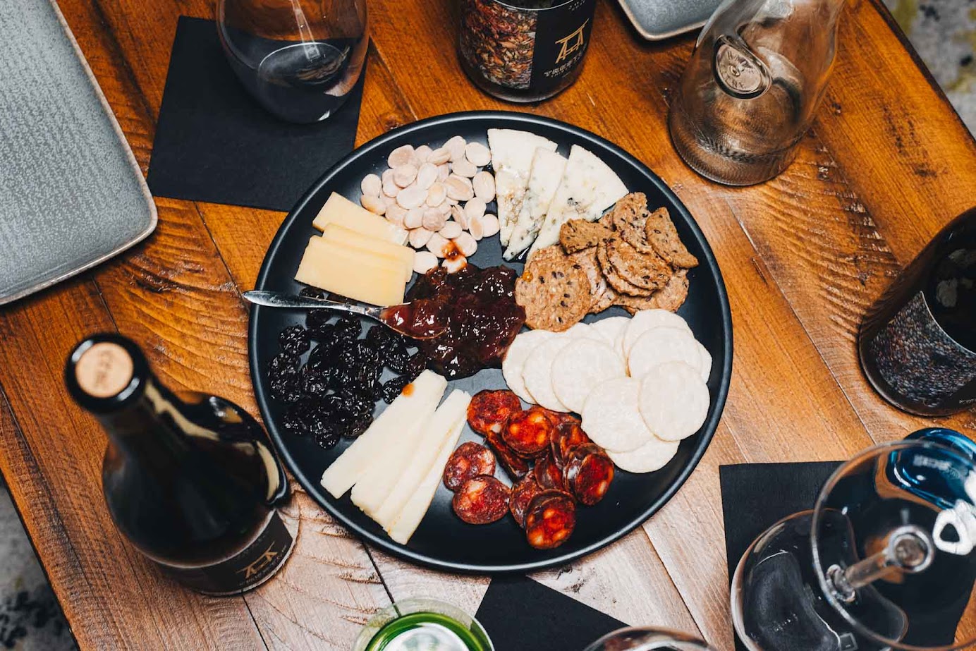 A charcuterie board with cheeses, crackers, meats, nuts, and jams on a wooden table with drinks from the best wineries in Finger Lakes.
