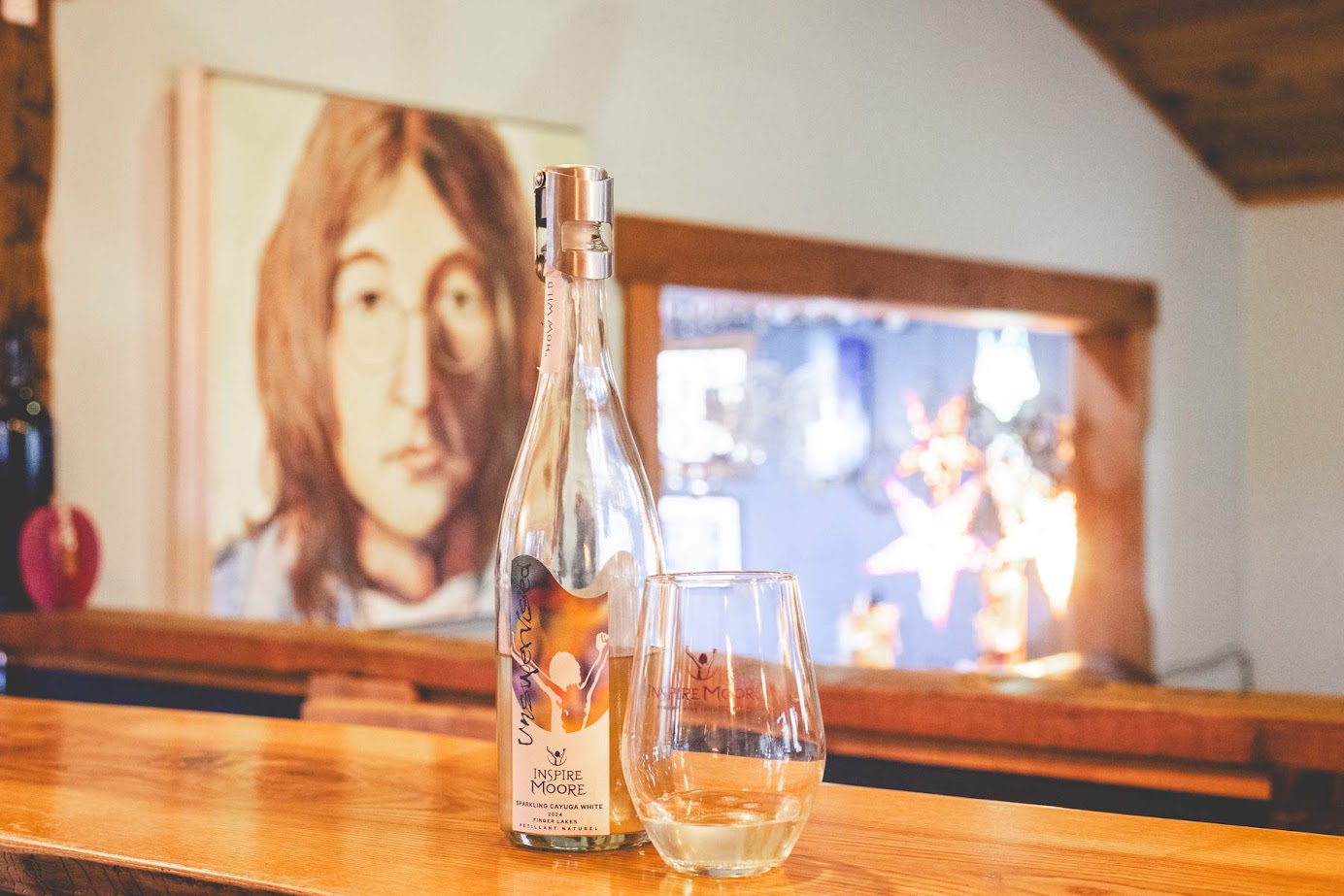 A wine bottle and a glass on a wooden counter with a blurry portrait in the background, capturing the cozy spirit of a Finger Lakes weekend getaway.