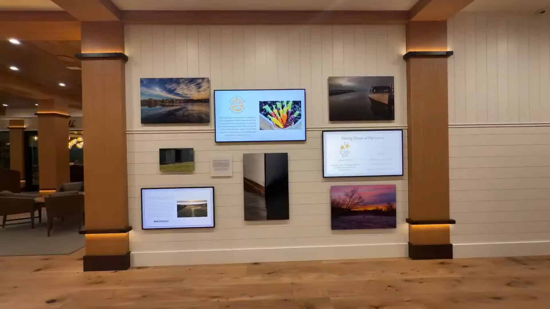 A wall display featuring screens, photos of Finger Lakes landscapes, and a mix of digital and printed informational panels highlights the serene ambiance of Skaneateles Fields Resort.
