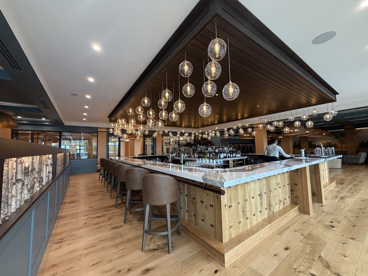 Modern bar with wooden accents, marble countertop, hanging glass lights, and empty barstools; perfect for a Finger Lakes fall road trip or weekend getaway. Bartender working behind the counter.
