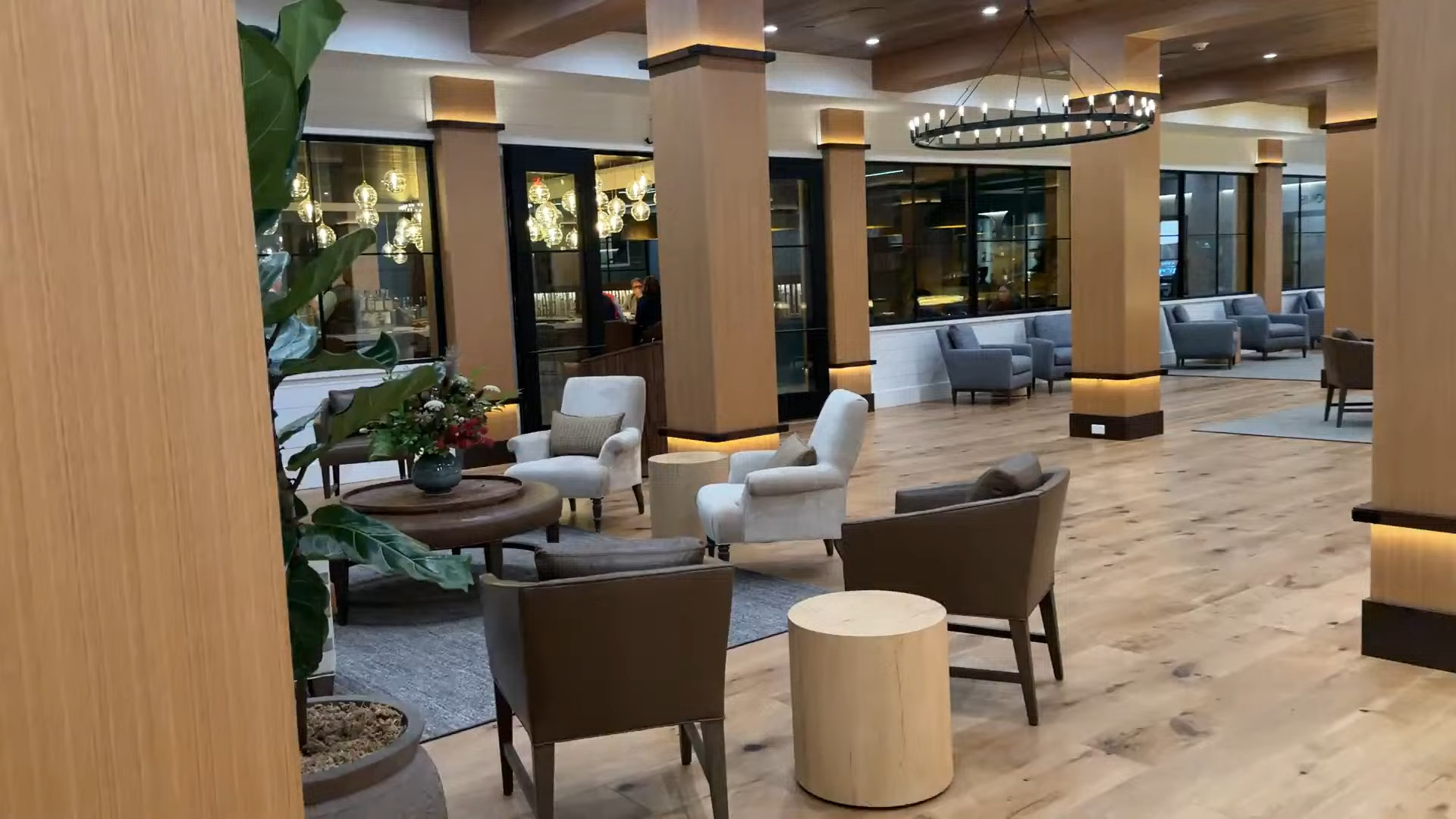 Modern hotel lobby with wood floors, armchairs, large windows, and a circular chandelier overhead at Skaneateles Fields Resort—a perfect welcome before you unwind at the spa or explore the scenic Finger Lakes.
