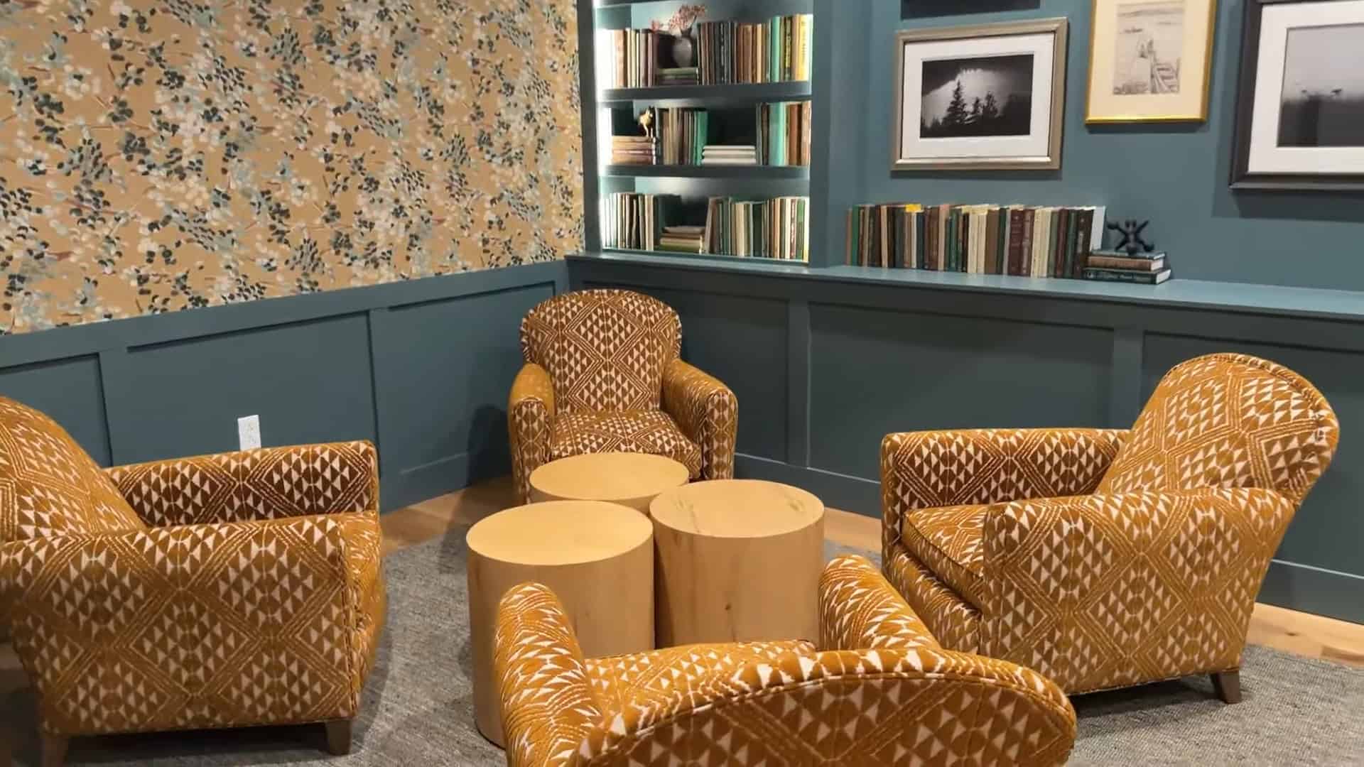 Cozy reading nook with four patterned armchairs, round wooden tables, bookshelves, and framed art on the wall—perfect for unwinding after a day at Skaneateles Fields Resort in the scenic Finger Lakes.