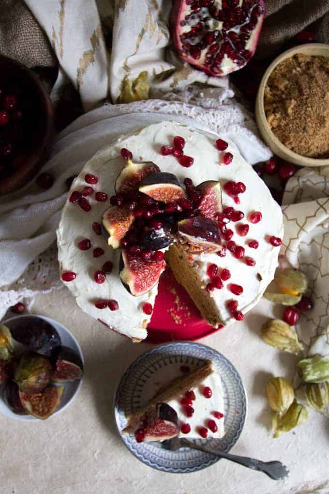 A frosted cake topped with figs and pomegranate seeds, reminiscent of the elegant vegetarian dishes in Russia, with a slice on a plate beside it.