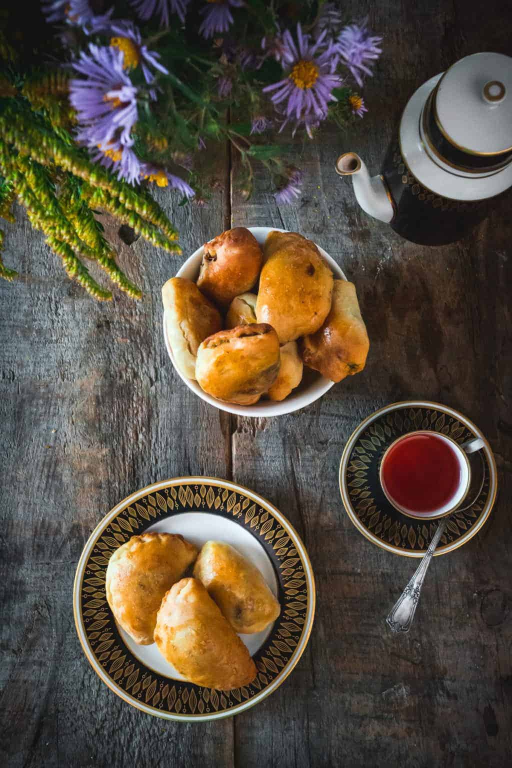 Baked pastries on a plate and in a bowl, with tea and flowers on a rustic wooden table, inspired by Top 13 vegetarian dishes from Ukraine.