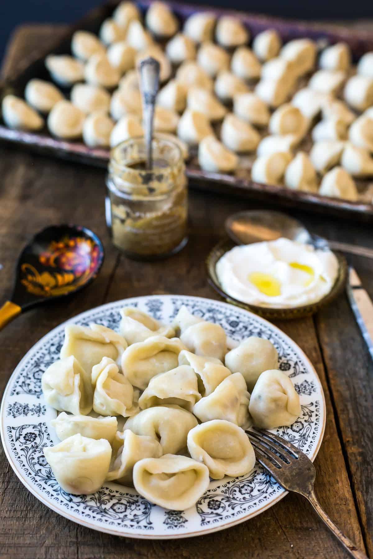 A plate of dumplings on a floral dish, with sour cream, mustard, and more dumplings in the background&mdash;a delicious example of vegetarian dishes in Russia.
