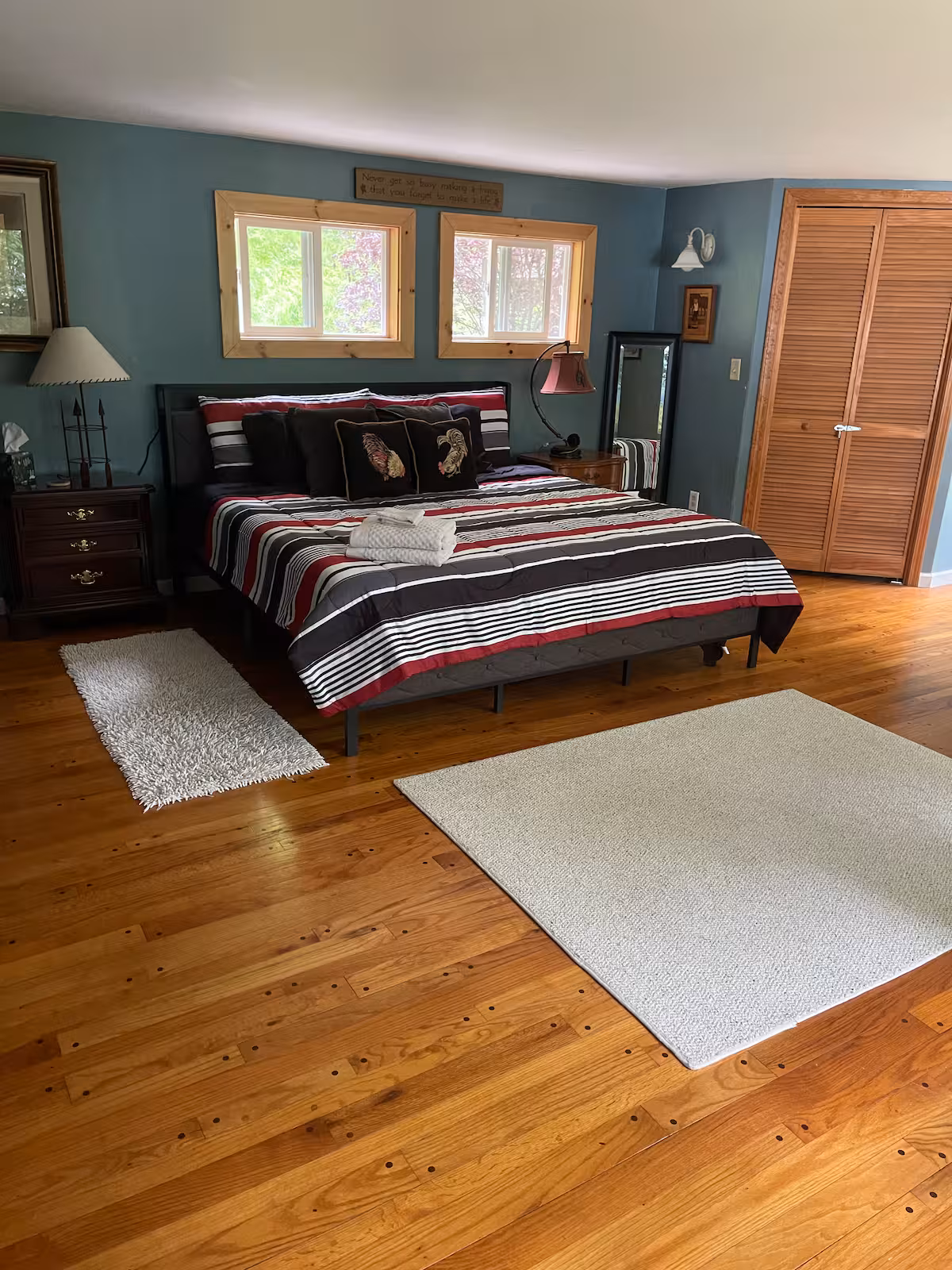 Bedroom with a striped bed, wood floor, rugs, nightstands, lamps, and double windows above the bed—perfect for relaxing in Finger Lakes vacation rentals or cozy cottages.