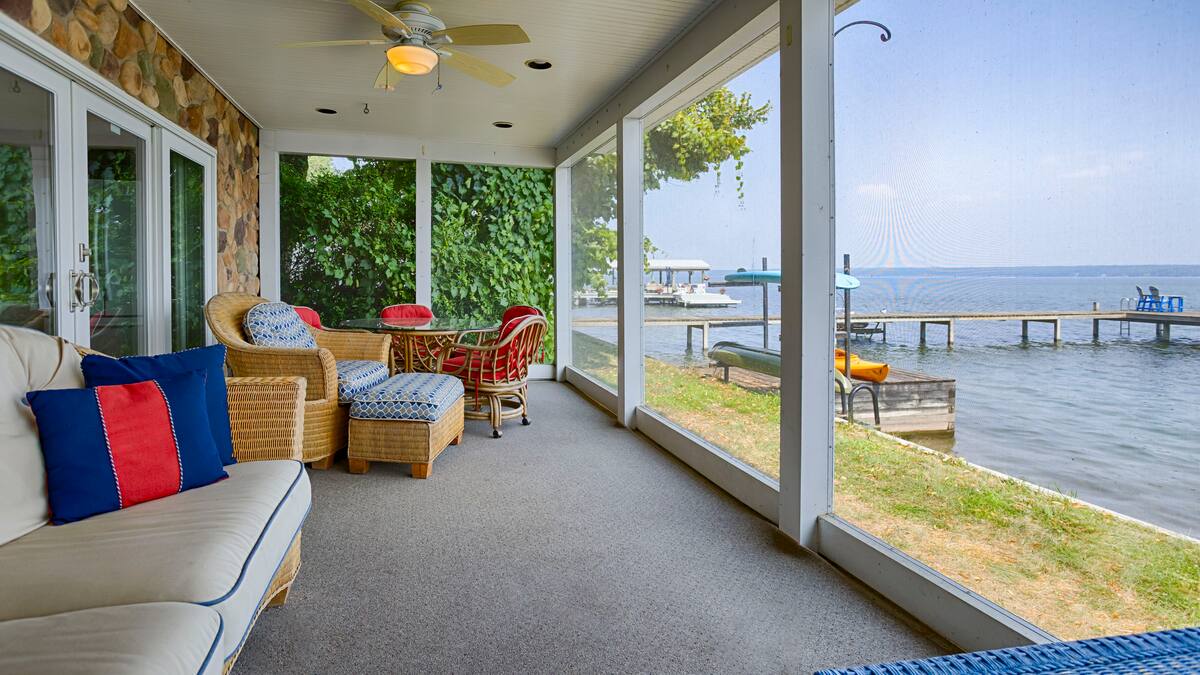 Screened porch with wicker furniture overlooking a lake, dock, and boats on a sunny day—perfect for relaxing at one of the charming Finger Lakes vacation rentals or cozy cottages.