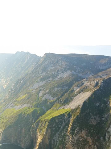 Steep green cliffs rising above the ocean under a bright, hazy sky.
