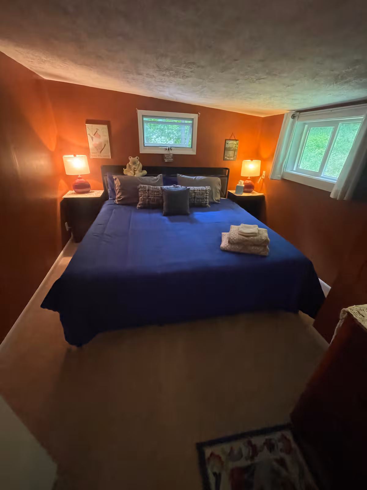 Cozy bedroom in one of our Finger Lakes Vacation Rentals, featuring a king bed with blue bedding, two lamps, windows, and folded towels on the bed—perfect for a relaxing stay in charming cabins or homes.