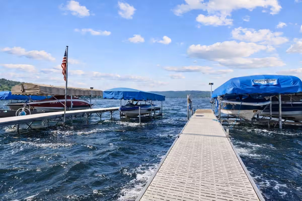 A dock extends into a choppy lake with boats covered by blue canopies on both sides under a sunny sky, perfect for enjoying Finger Lakes vacation rentals.