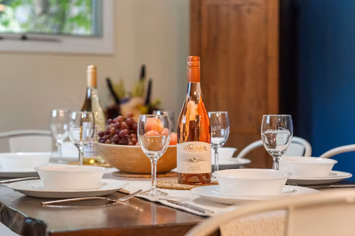 A dining table set with plates, wine glasses, a bottle of rosé, and a bowl of grapes awaits you in cozy Finger Lakes vacation rentals, perfect for relaxing stays in charming cottages or rustic cabins.
