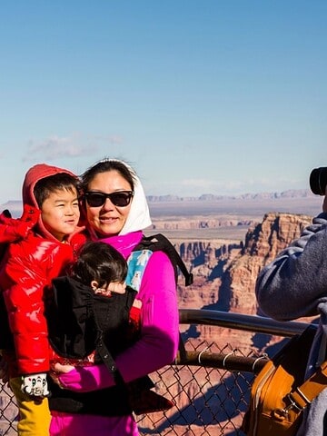 A person takes a photo of a woman and two children at a scenic Grand Canyon overlook on a sunny day.
