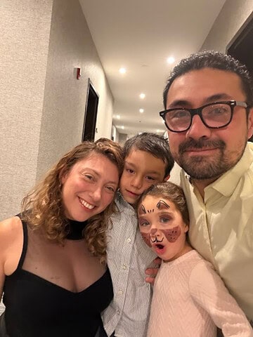 Four people smile in a hallway; one child has face paint resembling a cat, sharing excitement about exploring the Best Places to Stay in Finger Lakes Near Wineries.