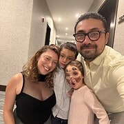 A smiling family of four poses in a hallway—one child has face paint—capturing a joyful moment during their visit to the Best Places to Stay in Finger Lakes Near Wineries.