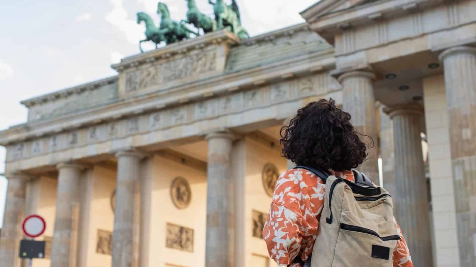 Person with a backpack facing the Brandenburg Gate in Berlin, viewed from behind on a sunny day.